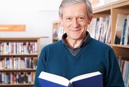 A man is reading a book in a library and smiling