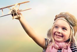 A little girl wearing a pilot hat and goggles is holding a toy airplane.