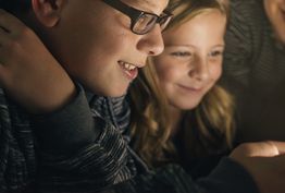 A boy and a girl are looking at a tablet together.