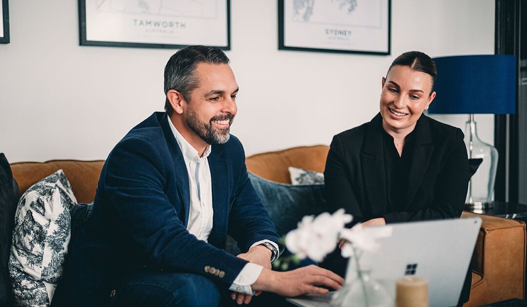 A Man and A Woman Are Sitting on A Couch Looking at A Laptop Computer — Slack-Smith Partners in Sydney, NSW