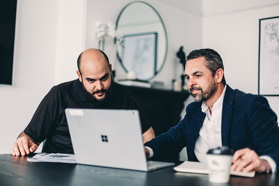 Two Men Are Sitting at A Table Looking at A Laptop Computer — Slack-Smith Partners in Tamworth, NSW