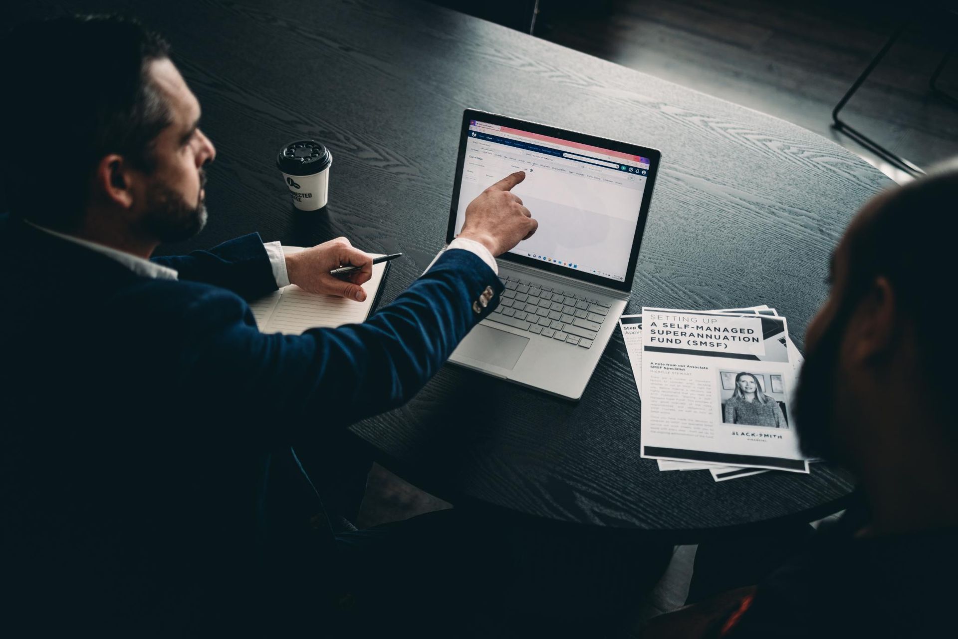 Two Men Are Sitting at A Table Looking at A Laptop Computer — Slack-Smith Partners in Tamworth, NSW