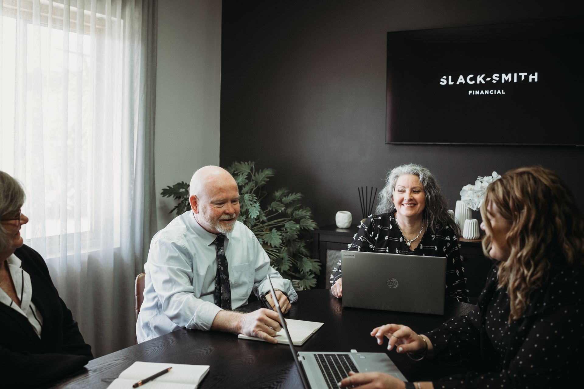 Four people in a meeting room, smiling and working at a dark table with laptops and notes. — Slack-Smith Partners in Gunnedah, NSW