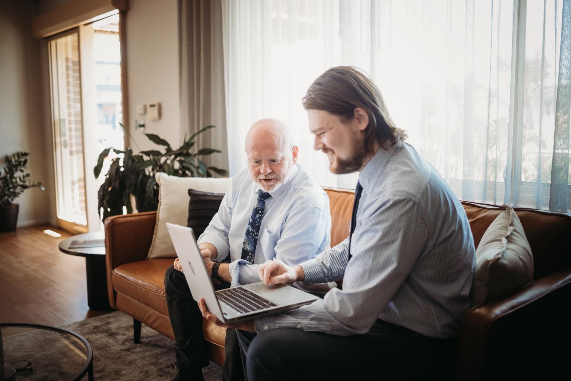Two Men Are Sitting on A Couch Looking at A Laptop — Slack-Smith Partners in Narrabri, NSW