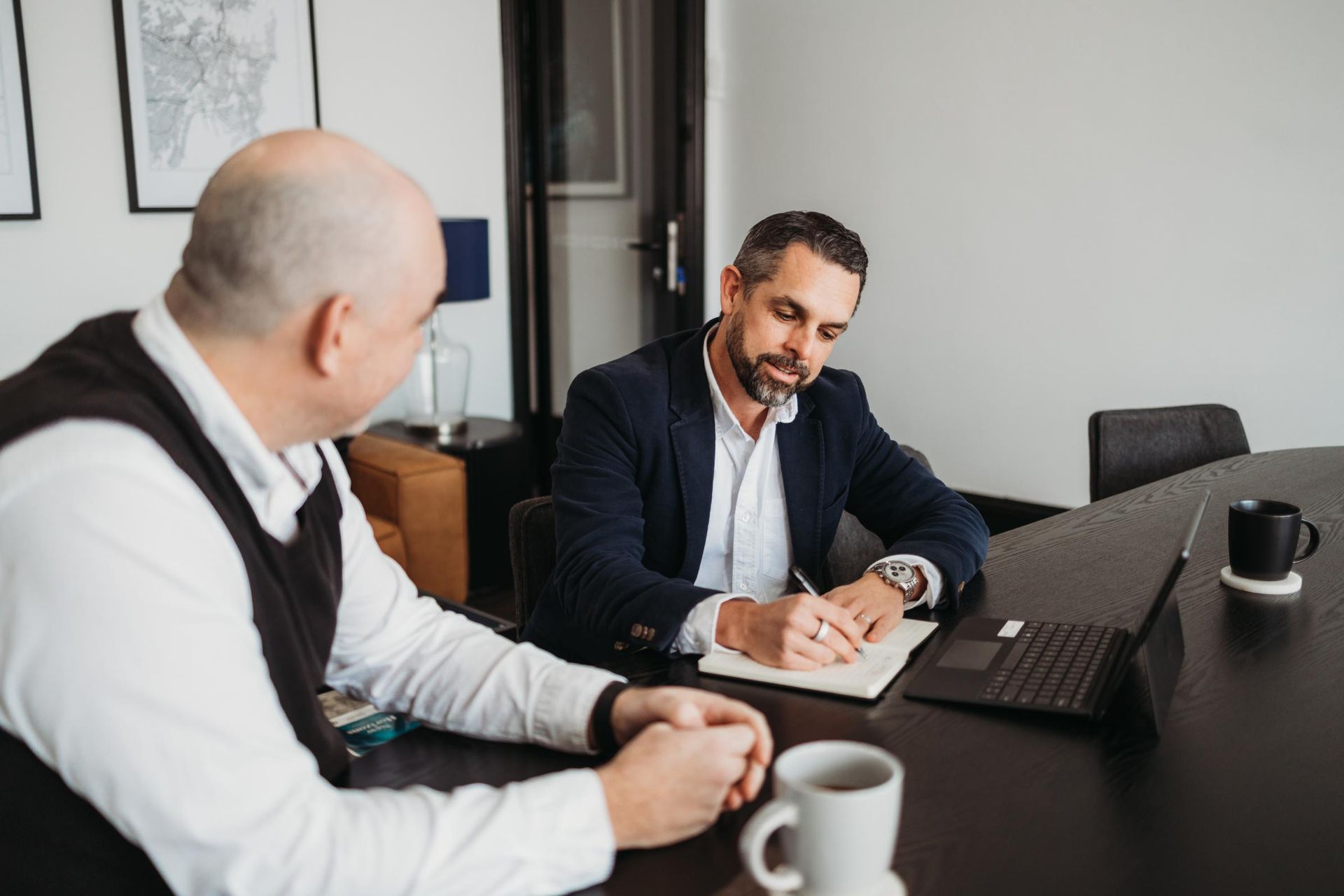 Two Men Are Sitting at A Table with A Laptop and A Notebook — Slack-Smith Partners in Tamworth, NSW