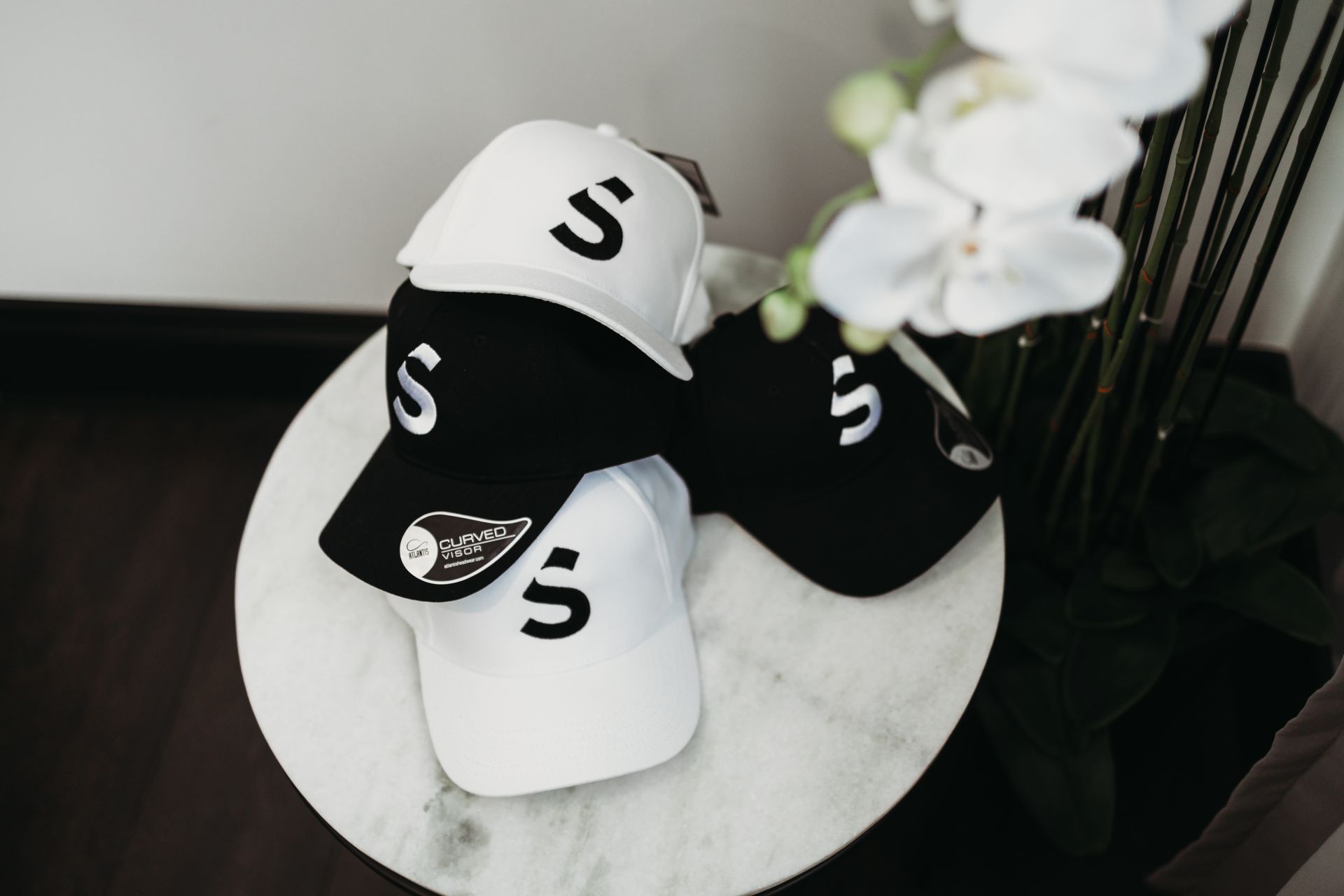 Four baseball caps, two black and two white, stacked on a marble-topped table. Each has a large