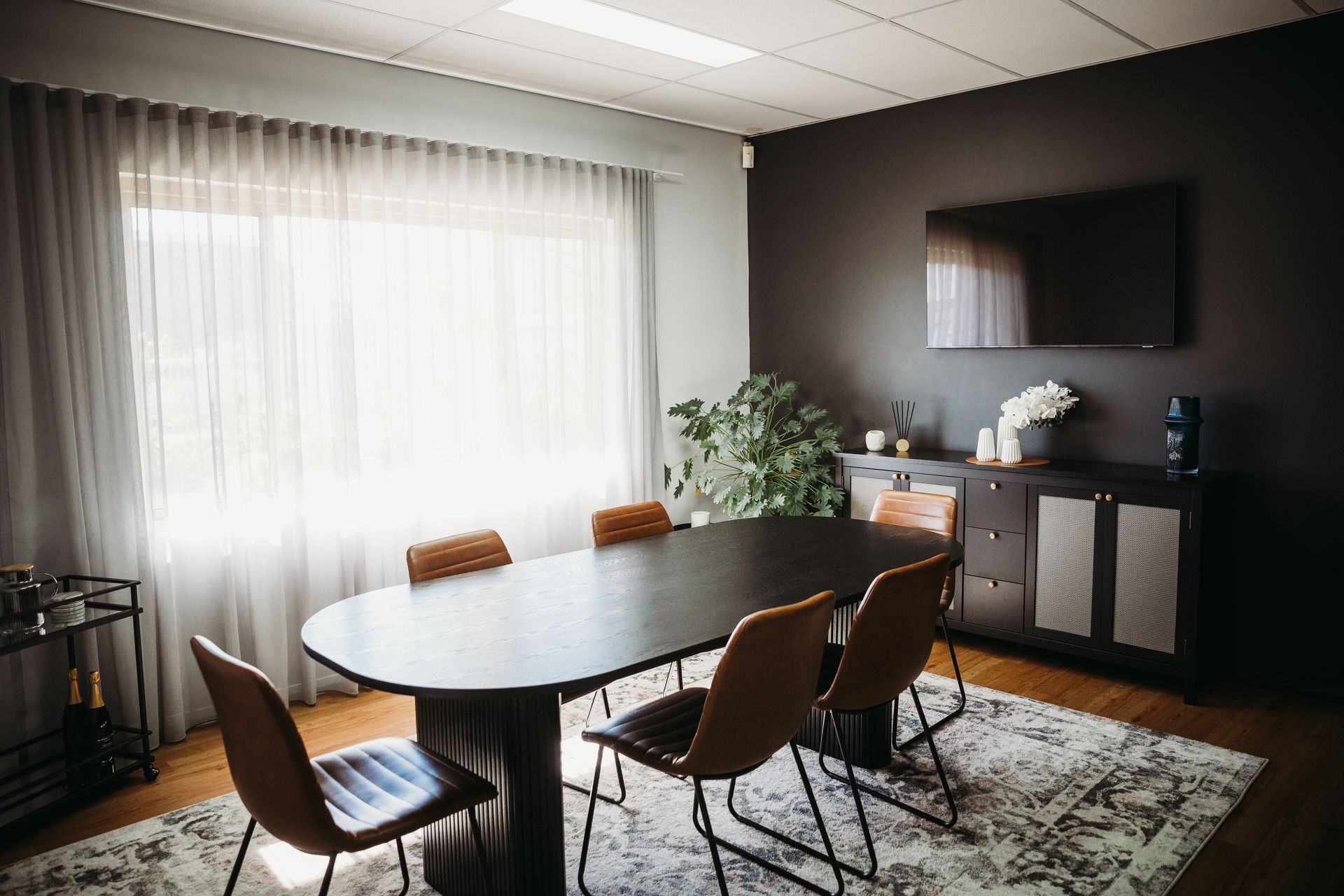 Meeting room with oval table, chairs, TV, window, dark walls, and area rug. — Slack-Smith Partners in Moree, NSW