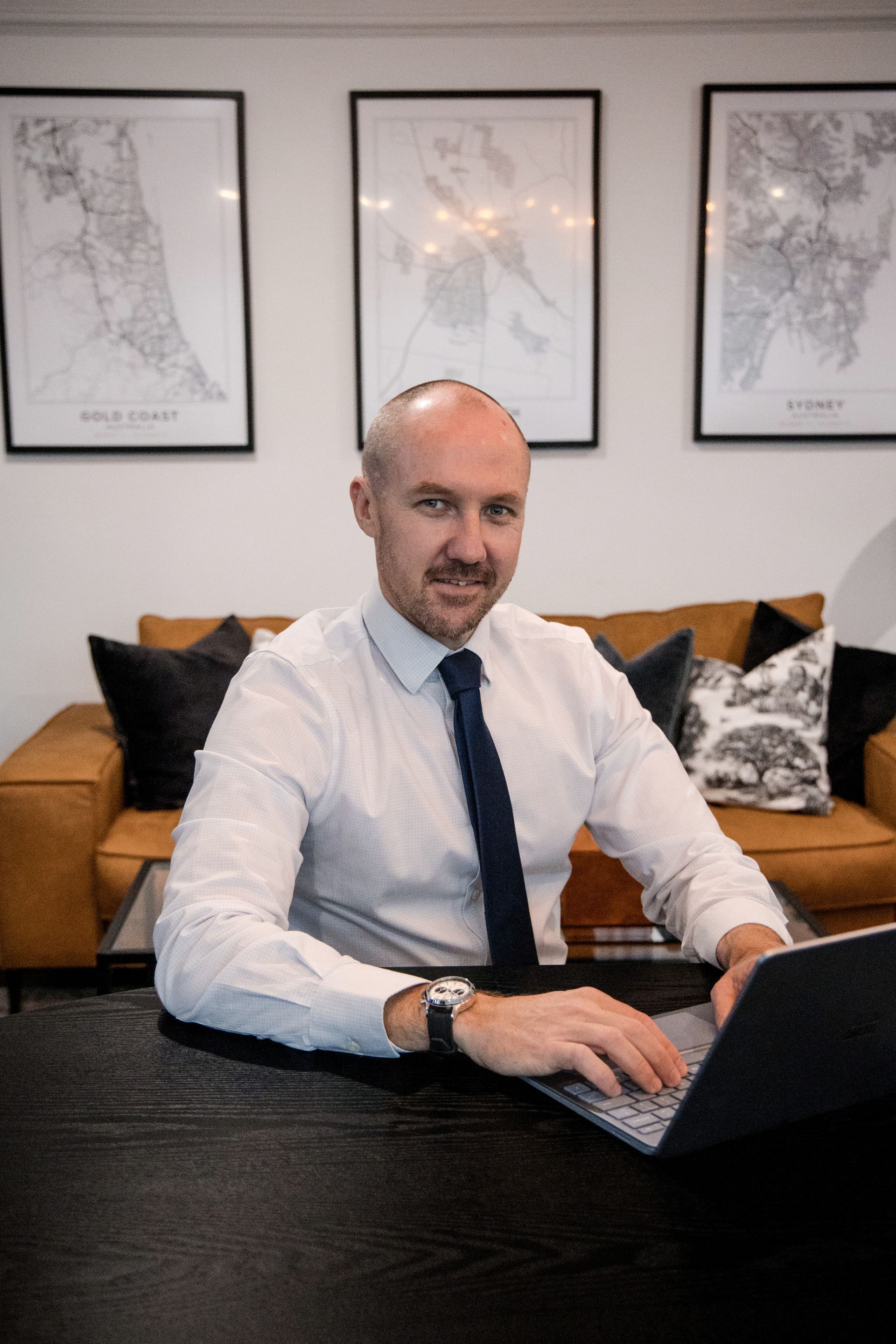 Man in White Shirt and Tie, Working on Laptop at Desk, Smiling. Brown Couch, Maps on Wall — Slack-Smith Partners In Moree, NSW