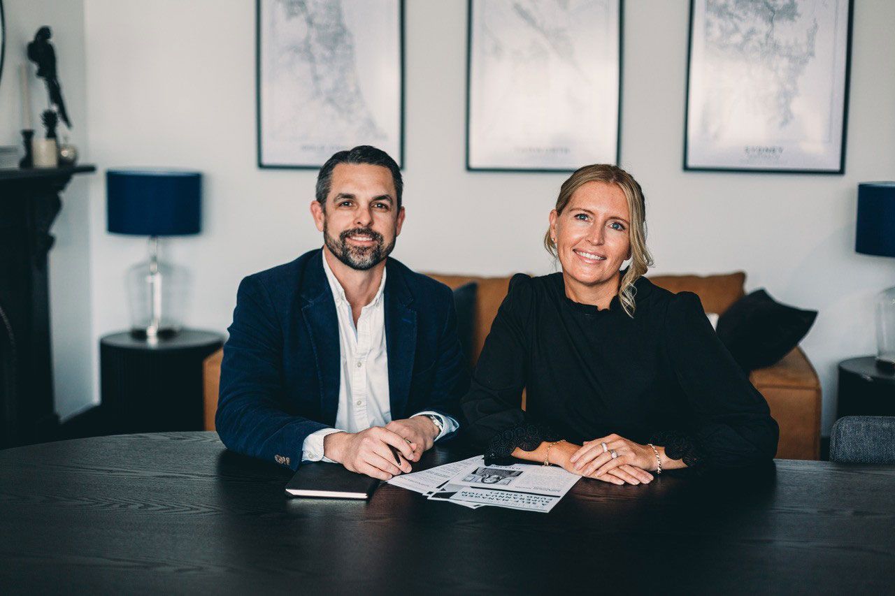 Woman in black dress holds an award, standing next to a man in a suit in front of a backdrop with 