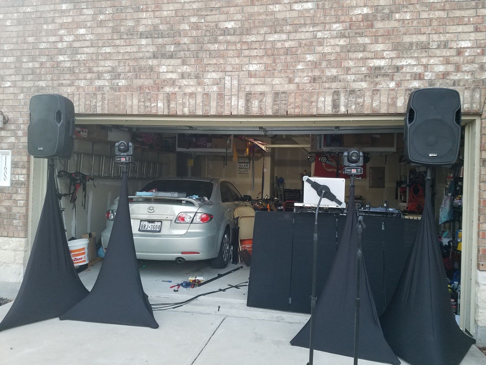 DJ setup in a garage: speakers, equipment on stands, and a silver car inside the garage.