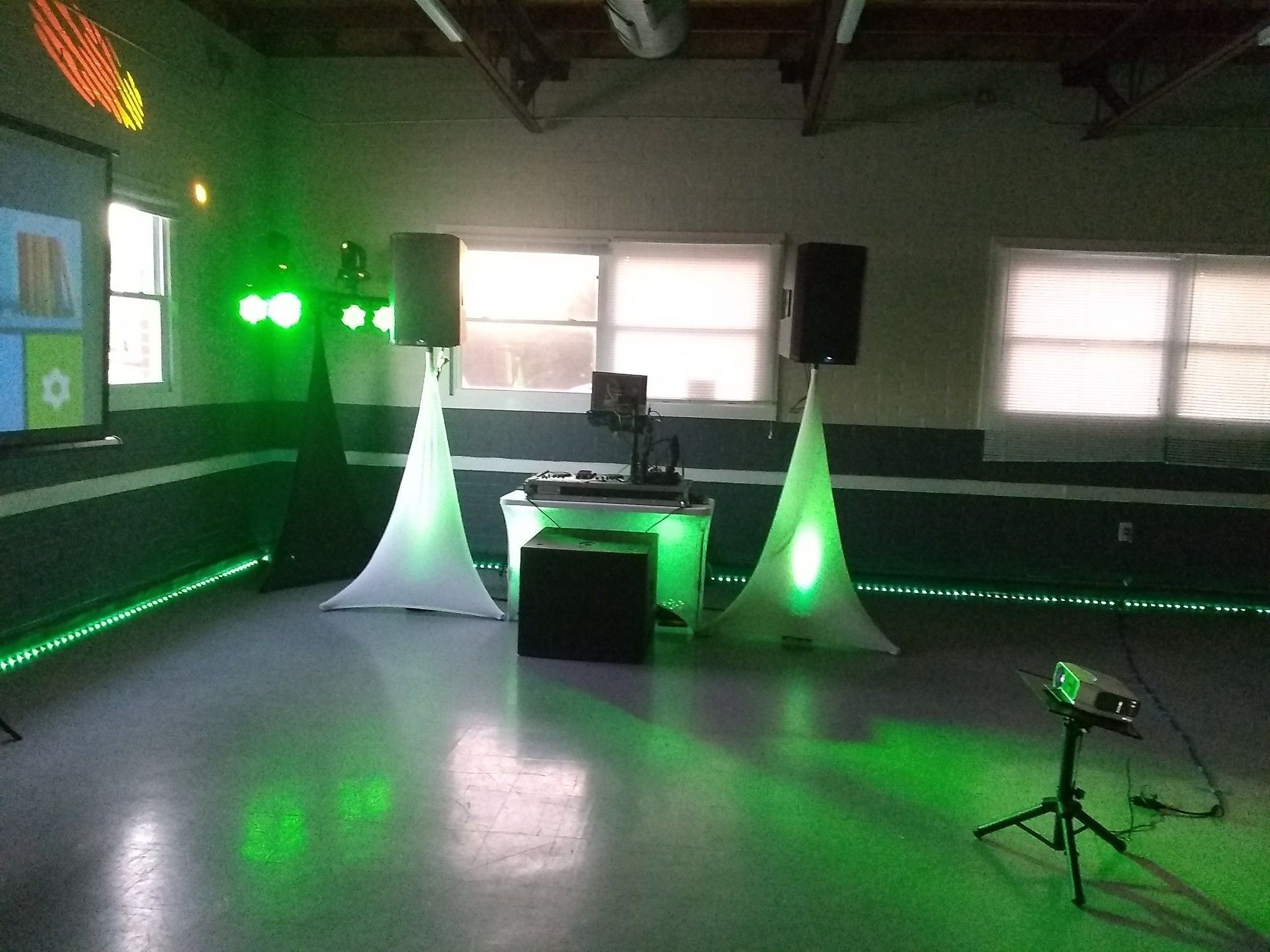 DJ setup with speakers, lights, and a projector illuminating a room in green.