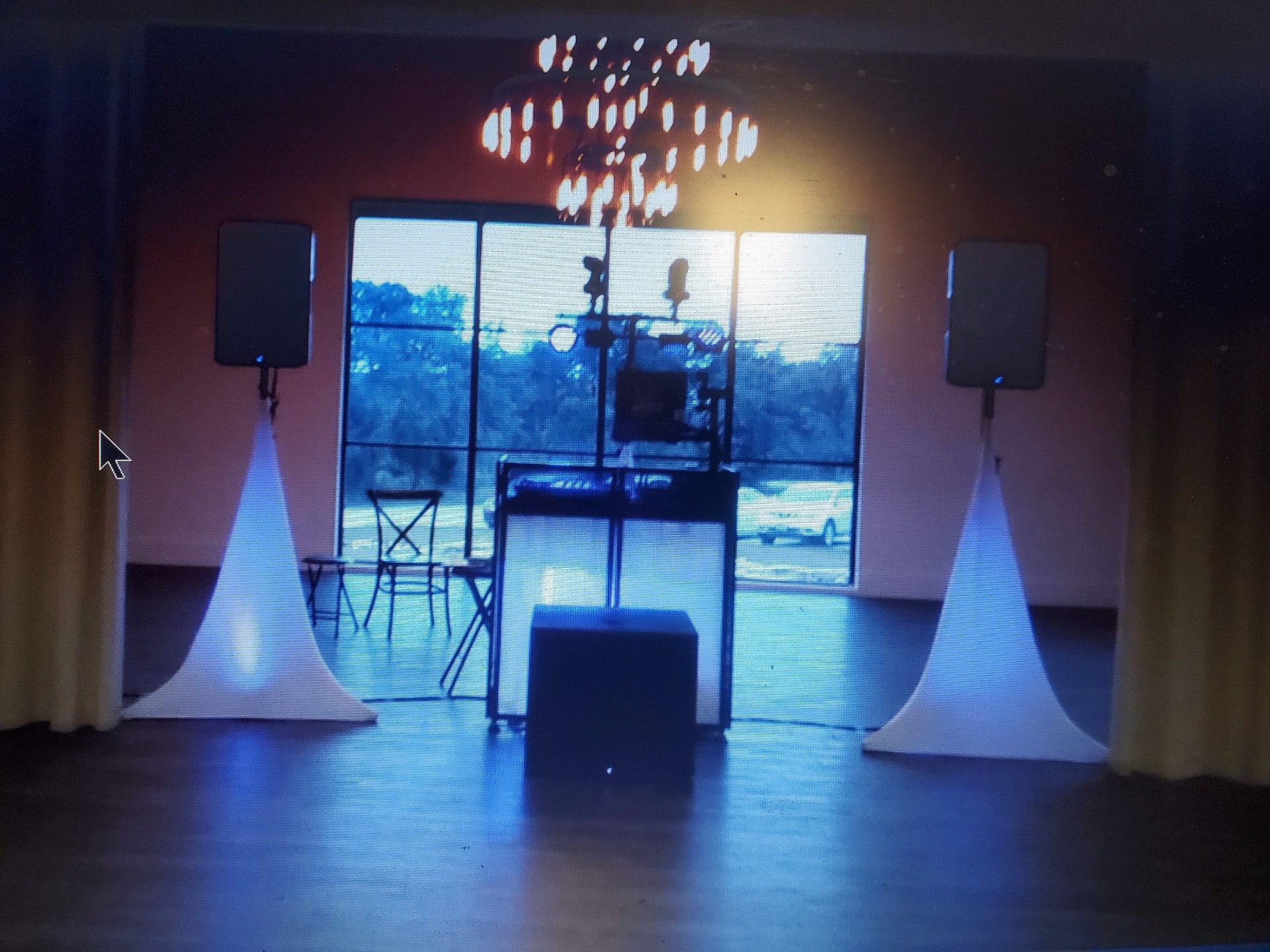 DJ setup with speakers, lighting, and equipment, set in front of a window.
