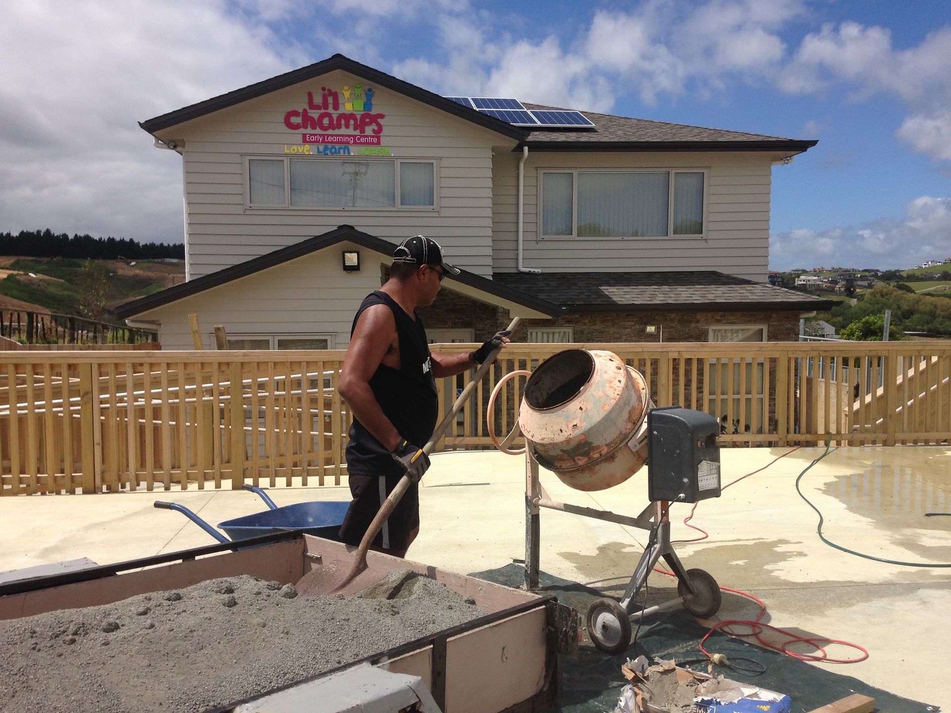 Man using a cement mixer on a rooftop, with a building in the background.