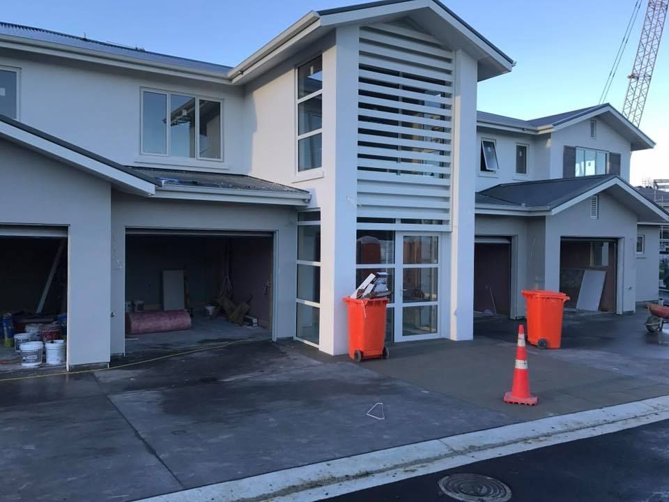 New townhouses under construction, with open garages, grey exteriors, and orange trash cans.