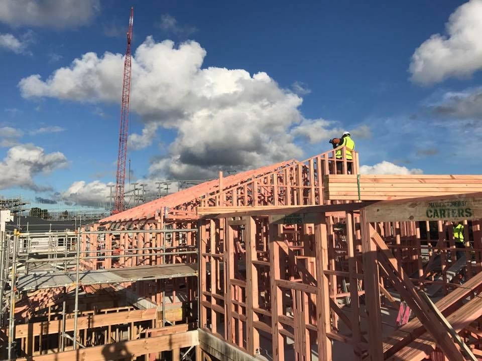 Construction workers on a partially built building frame under a cloudy sky. A crane is visible in the background. Construction workers on a partially built building frame under a cloudy sky. A crane is visible in the background.