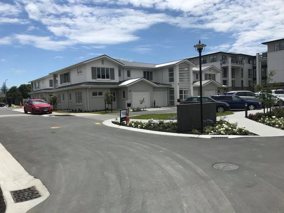 Gray buildings with garages, landscaped entrance, cars parked, and a cloudy sky. Gray buildings with garages, landscaped entrance, cars parked, and a cloudy sky.