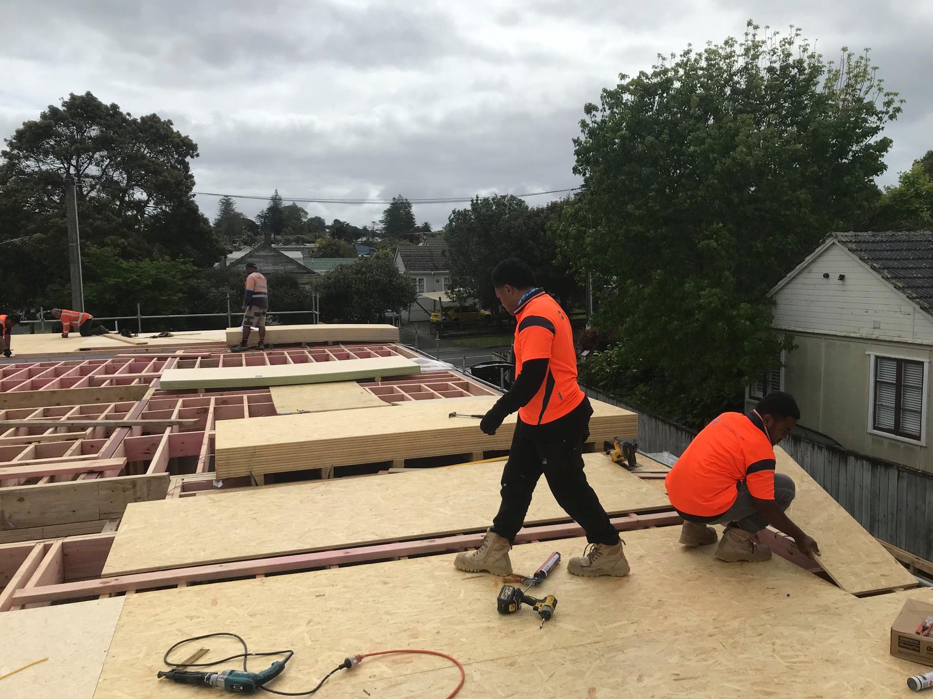 Construction workers installing plywood sheeting on a roof under overcast skies.