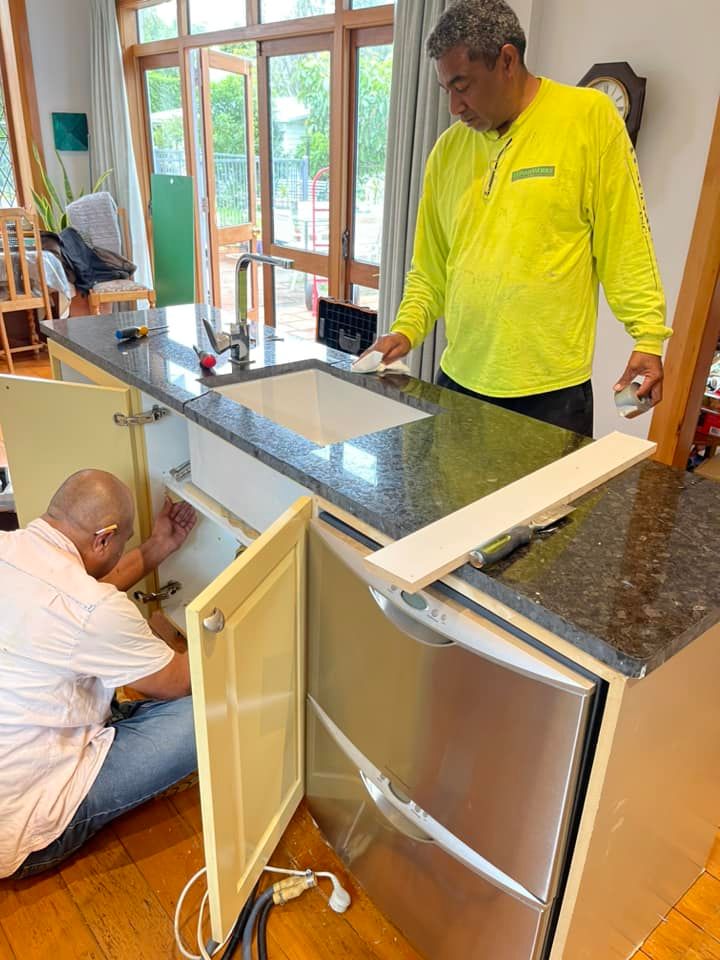 Two men installing a kitchen island with a granite countertop, and sink. One is working inside the cabinet. The other is looking on.