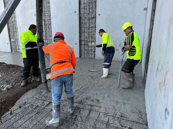 Construction workers pouring concrete on a foundation. Men are wearing safety vests and boots, using tools.