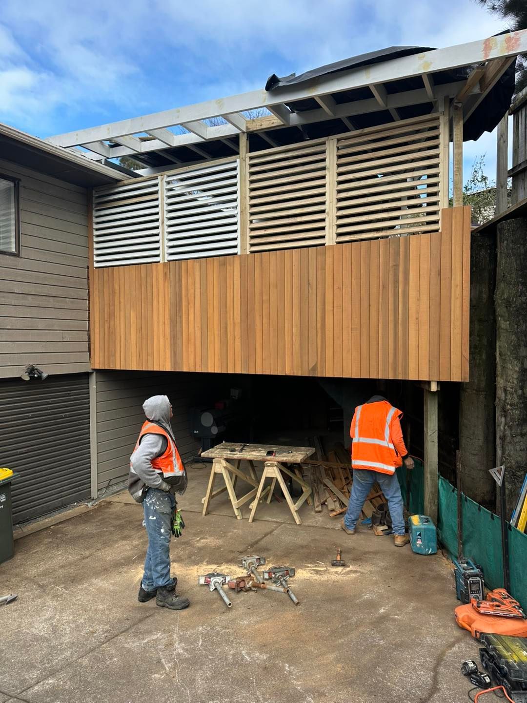 Construction workers on site building a wooden deck with a slatted privacy screen.