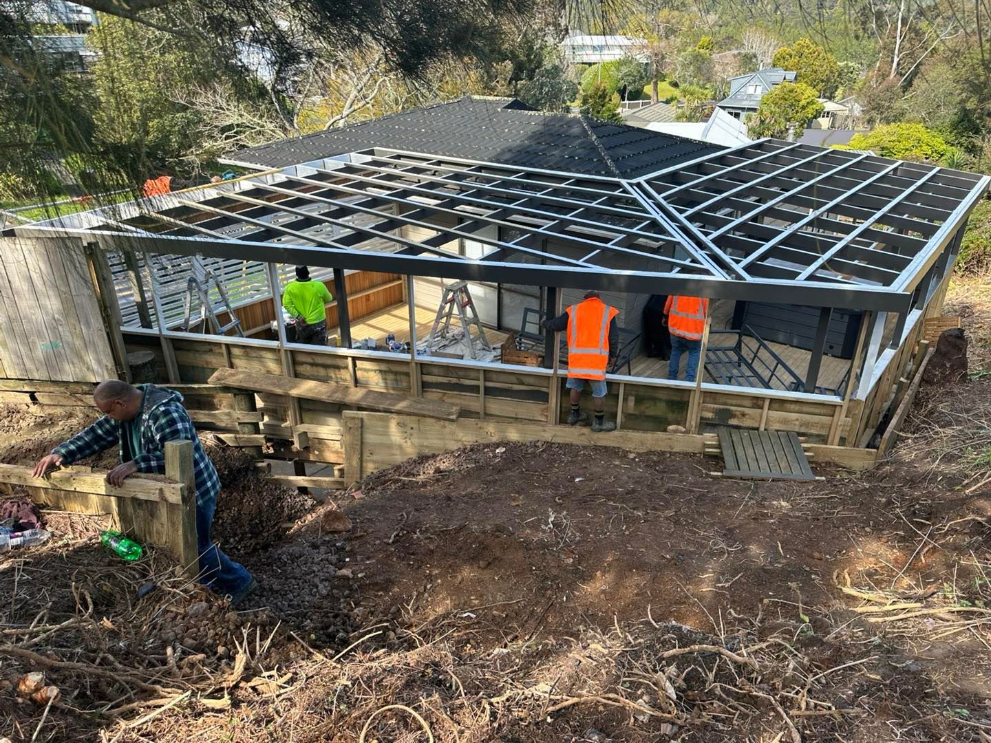 Construction workers building a structure with a dark roof on a hillside.