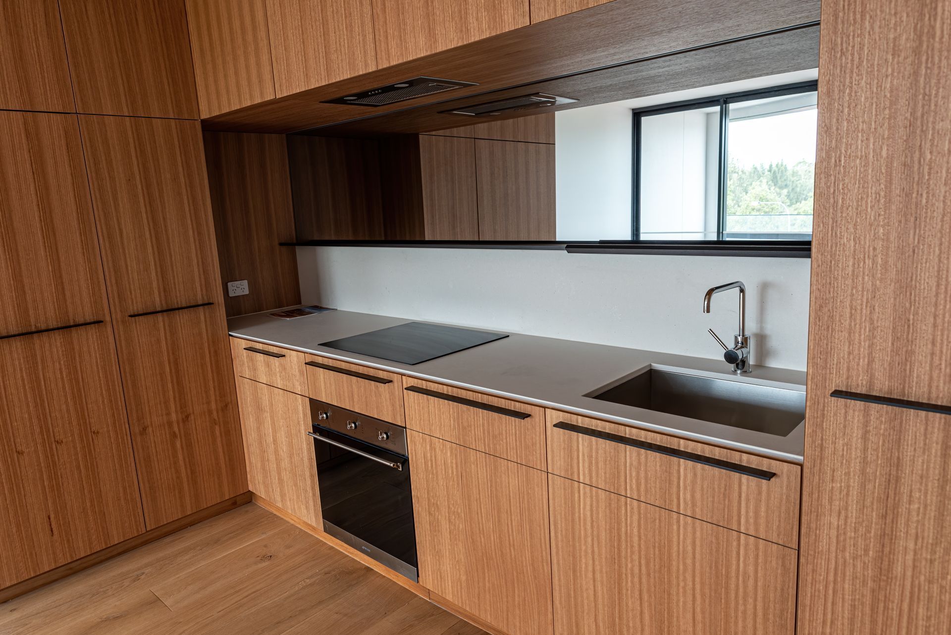 Modern kitchen with wood cabinets, gray countertop, black appliances, and a window.