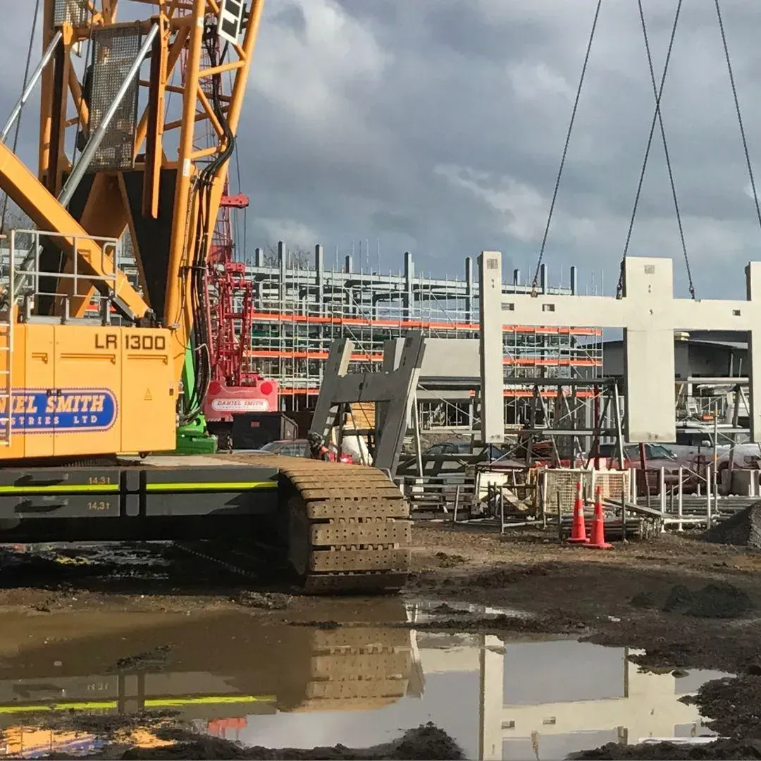 Construction site with a large yellow crane lifting a concrete building component.