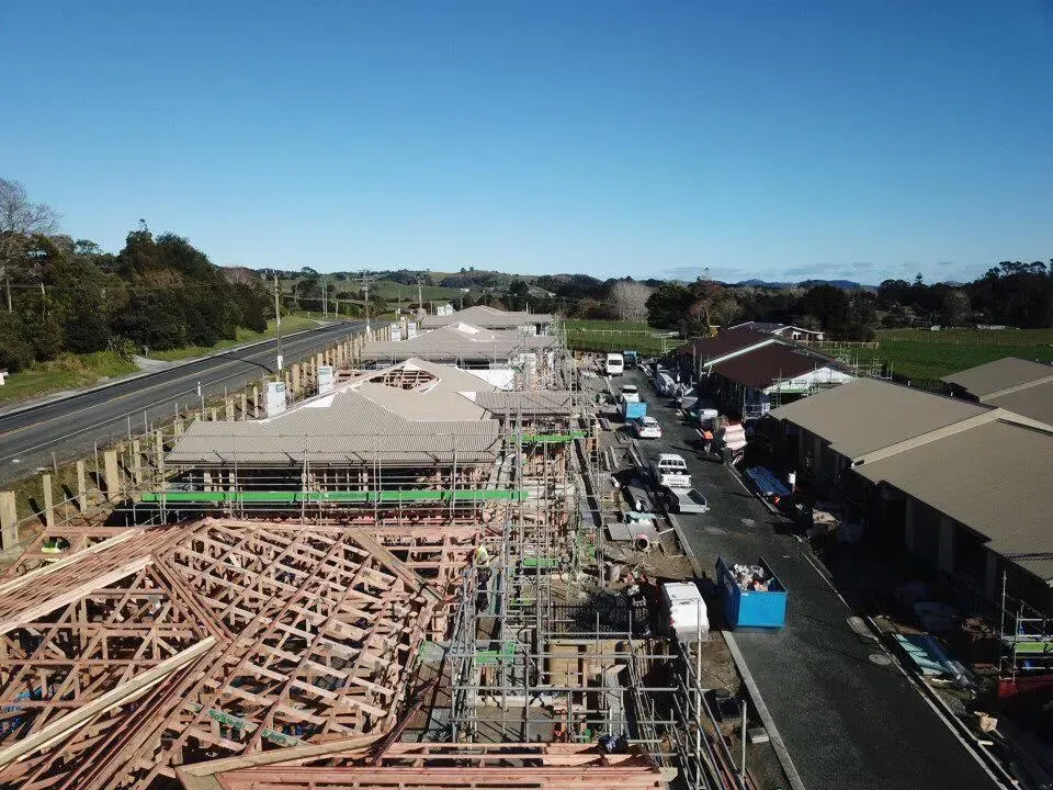 Construction site with unfinished buildings, trucks, and materials under a blue sky.