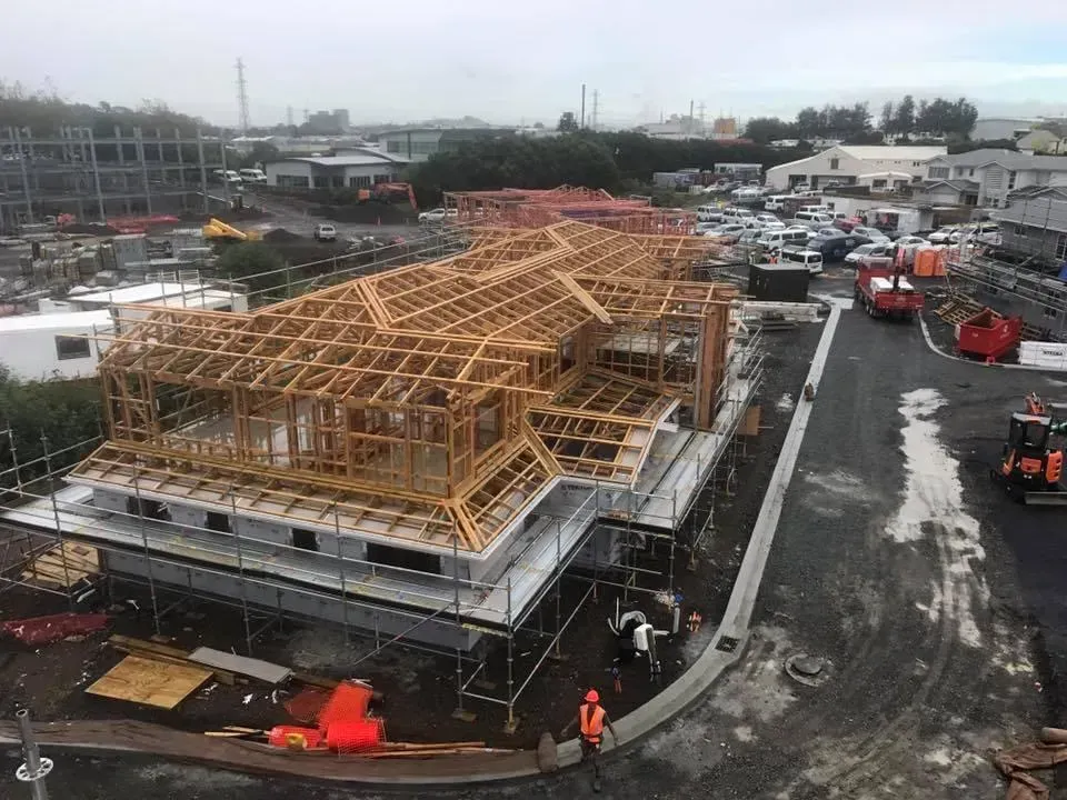 Construction site with wooden framework of a house. Workers, trucks, and equipment visible. Overcast day.