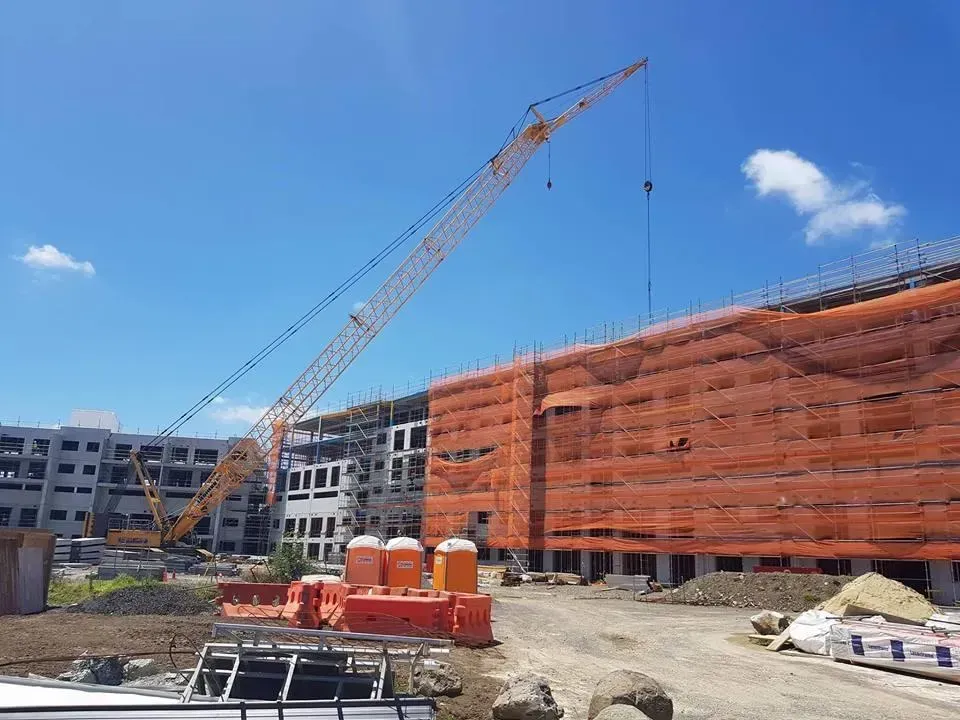 Construction site with a tall crane next to a building covered in orange netting under a bright blue sky.