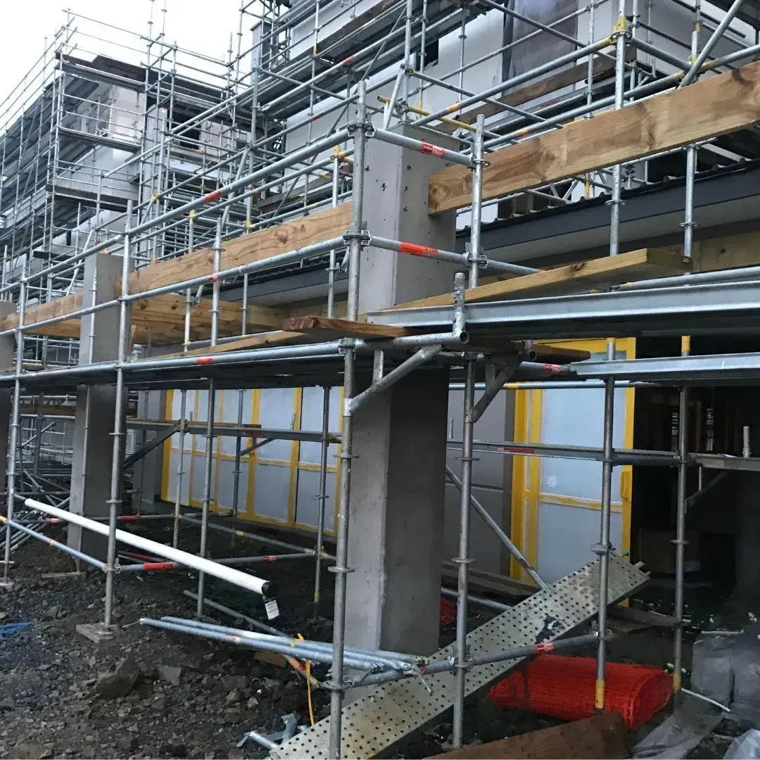Scaffolding surrounds a building under construction, with wooden planks and metal supports.