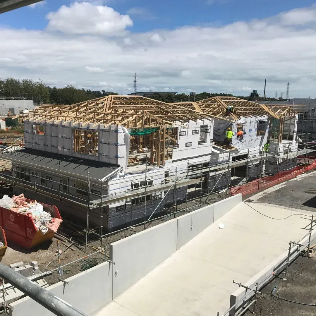 Multi-unit residential construction site with exposed wooden roof frames and wrapped walls, blue sky.