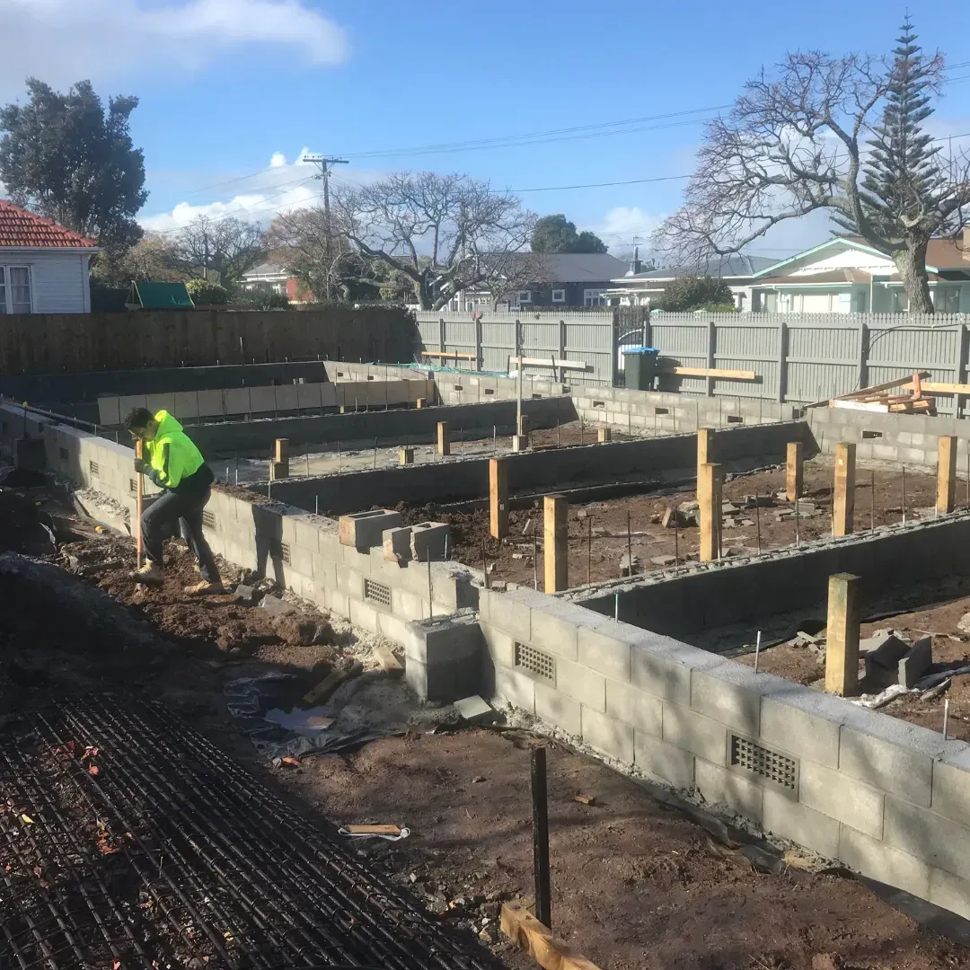Construction site with concrete block foundation, worker, and timber supports.