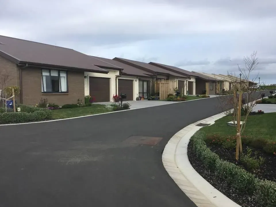 Row of brick houses with brown roofs and garage doors, on a paved road under a cloudy sky.