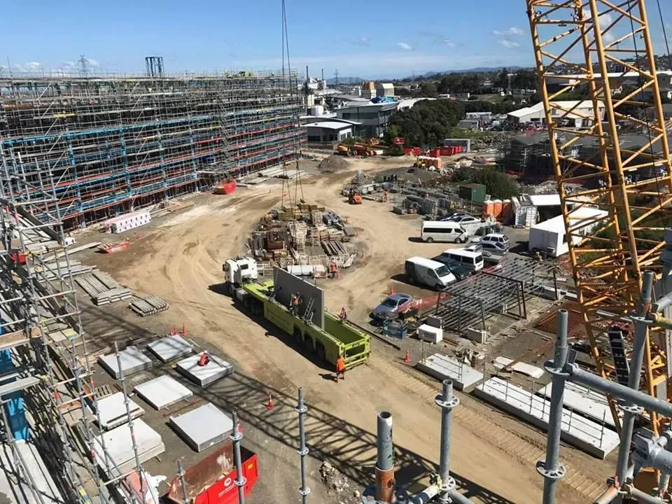Construction site with large unfinished building, crane, trucks, and materials.