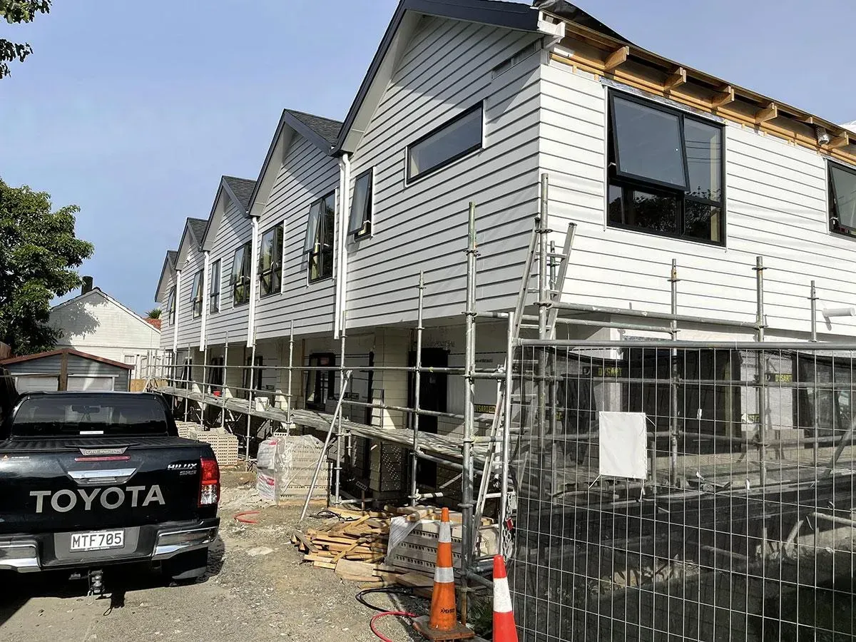 Row of new townhouses under construction, white siding, black windows, with scaffolding and a Toyota truck.