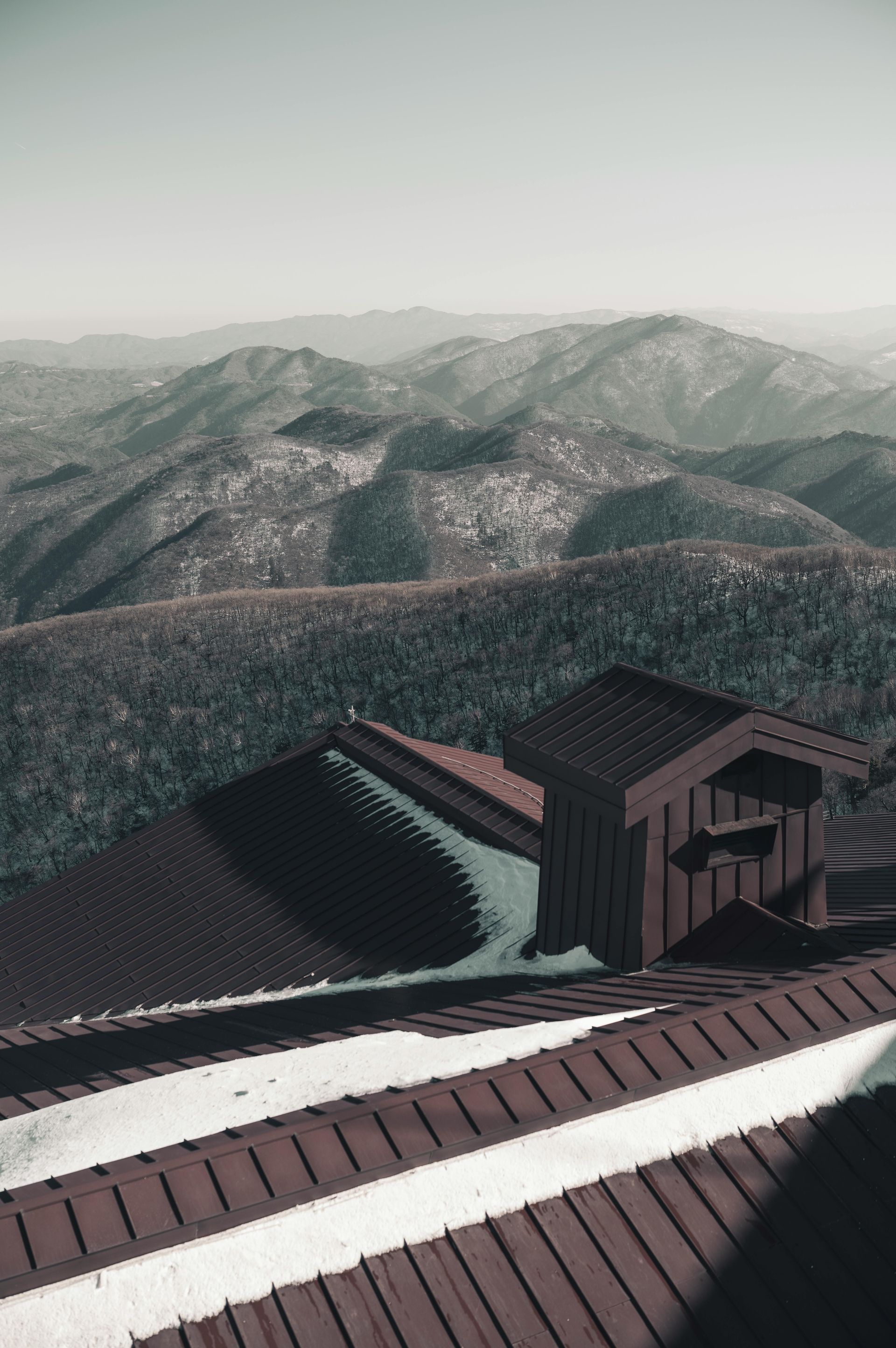 Roof of a building overlooking a mountainous landscape with snow patches.