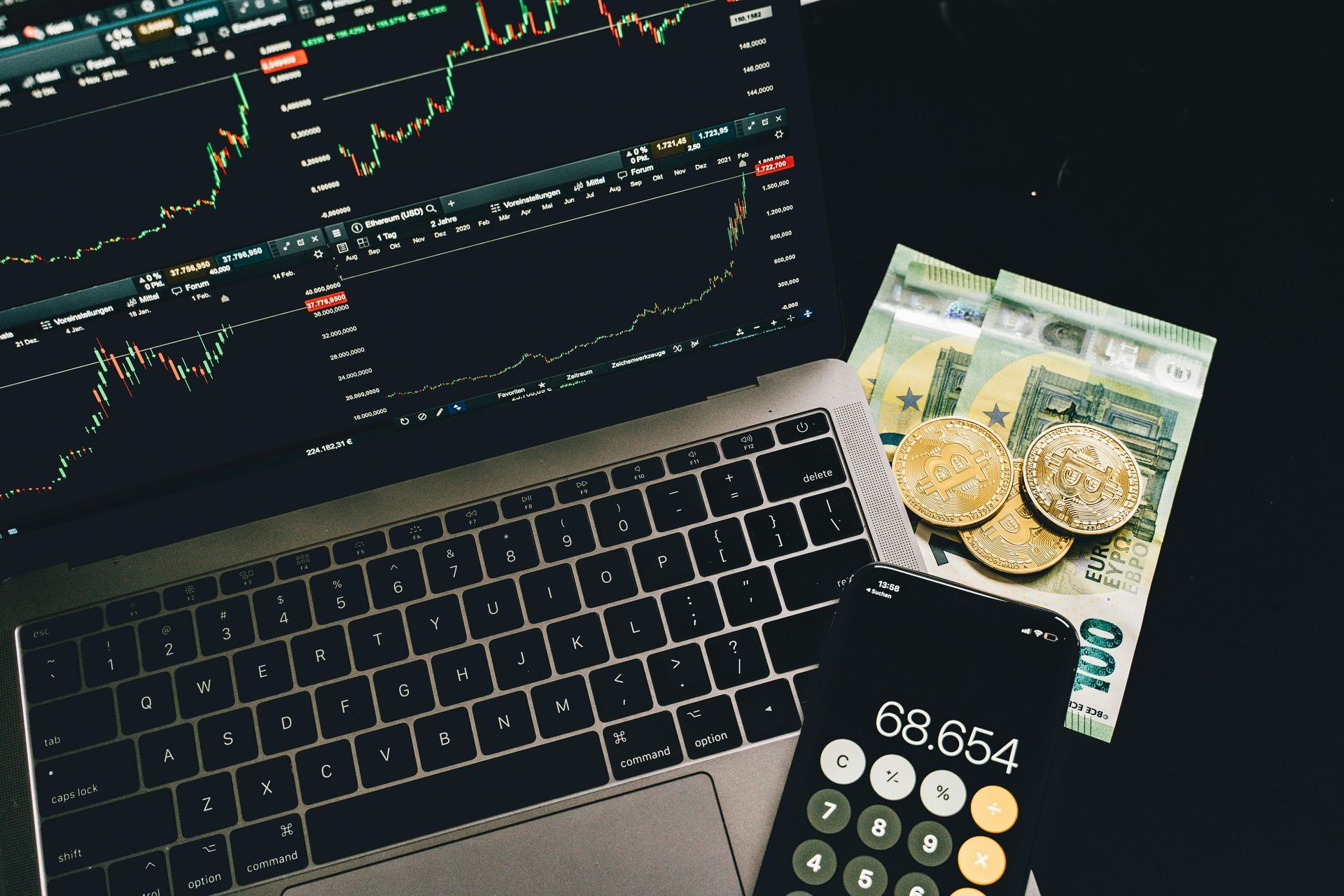 Laptop with trading charts, cash, coins, and a calculator on a desk