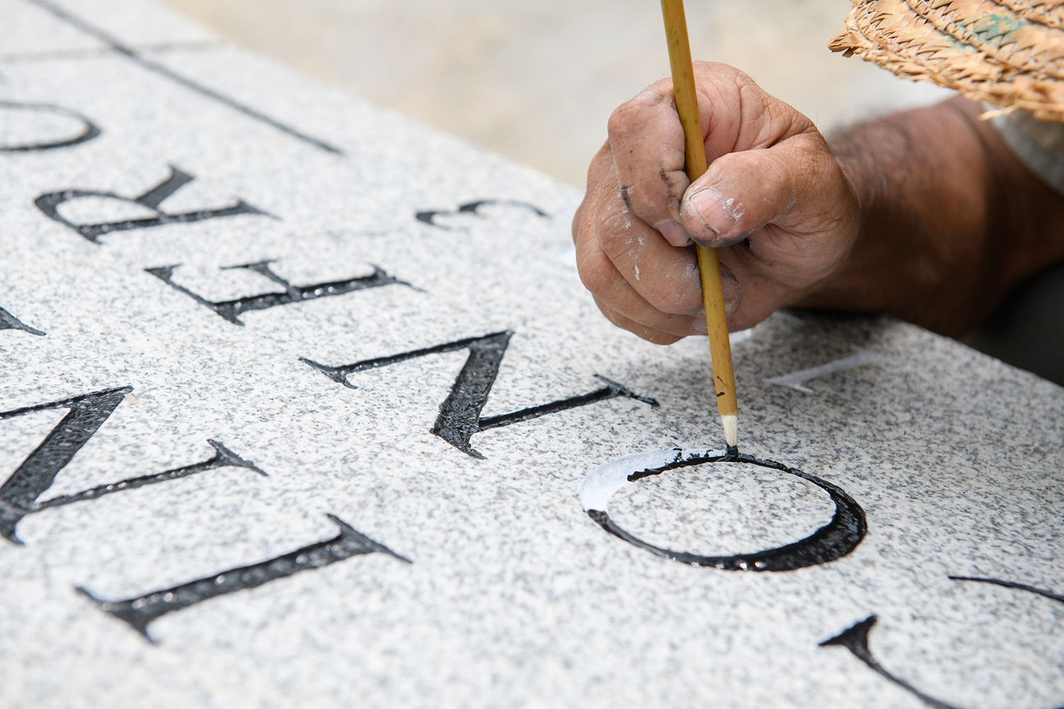 A headstone maker with a small brush making final touches to a headstone.