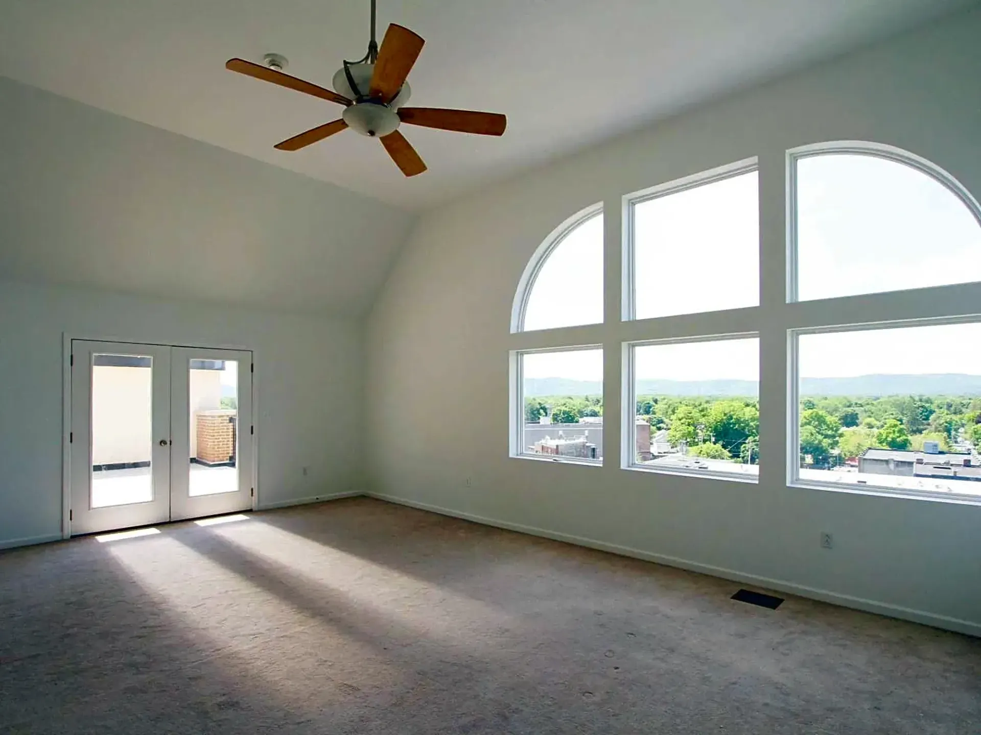 An empty room with arched windows and a ceiling fan