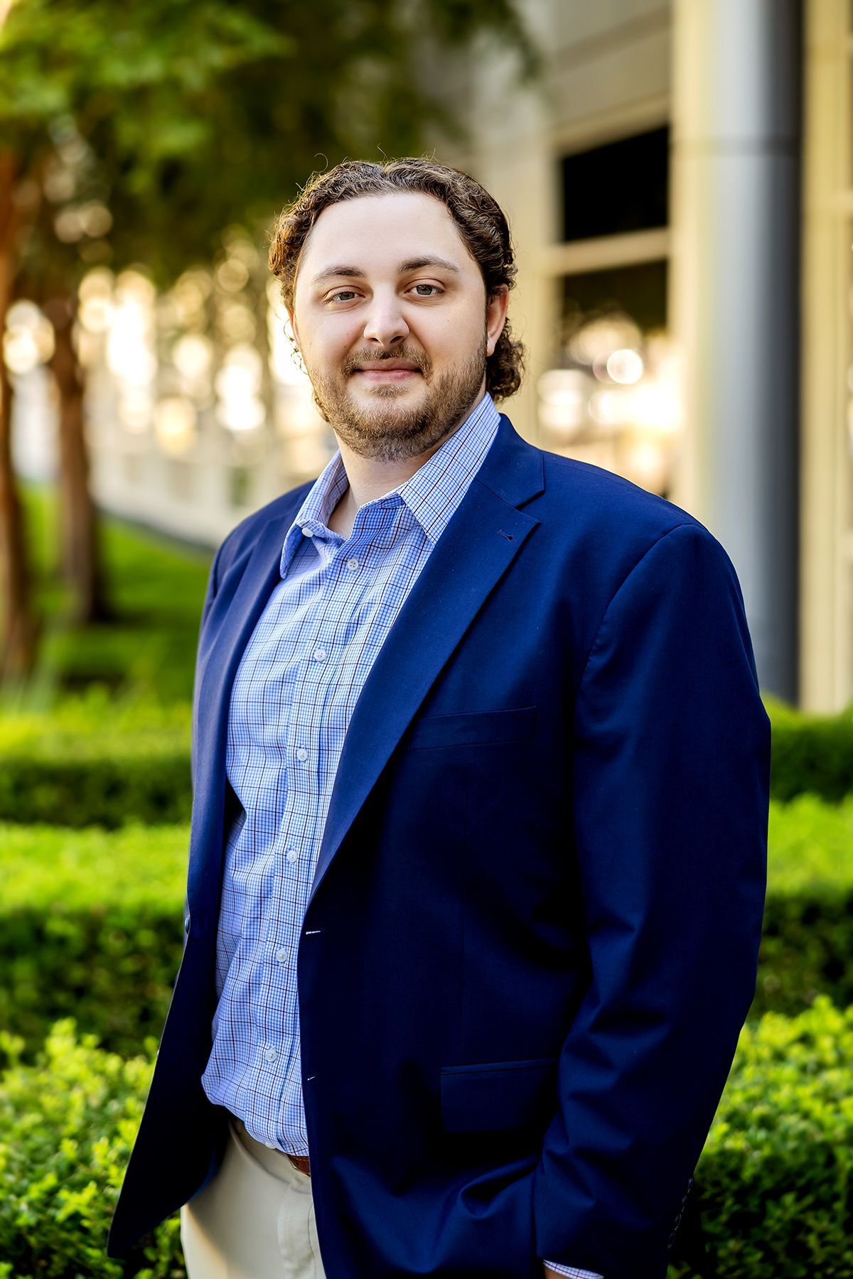 Man in blue blazer and shirt smiles in front of a building.