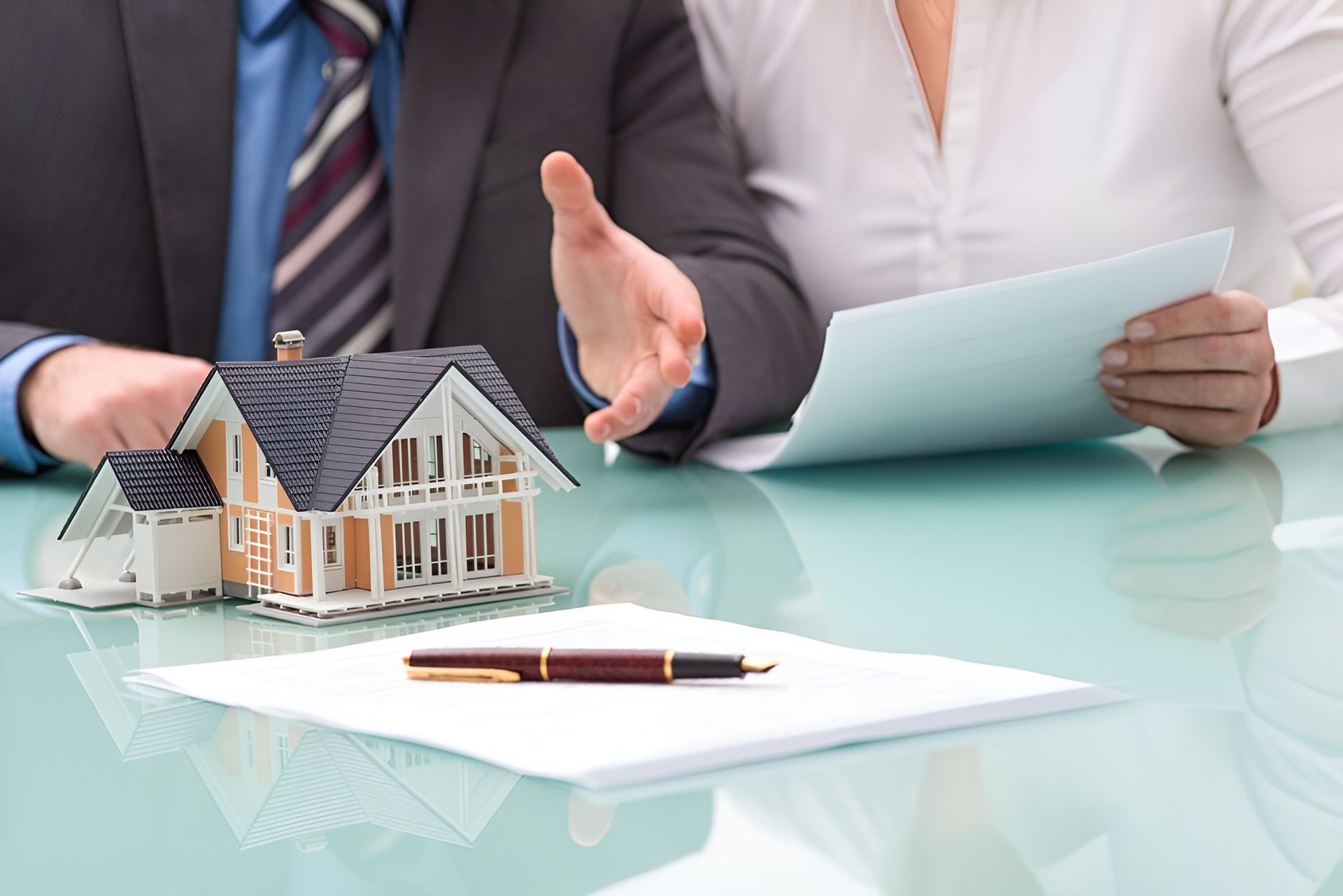 A real estate agent gestures toward a miniature house model on a table with a contract and a pen — Murphy Finance Solutions–Darwin & Palmerston In Zuccoli, NT