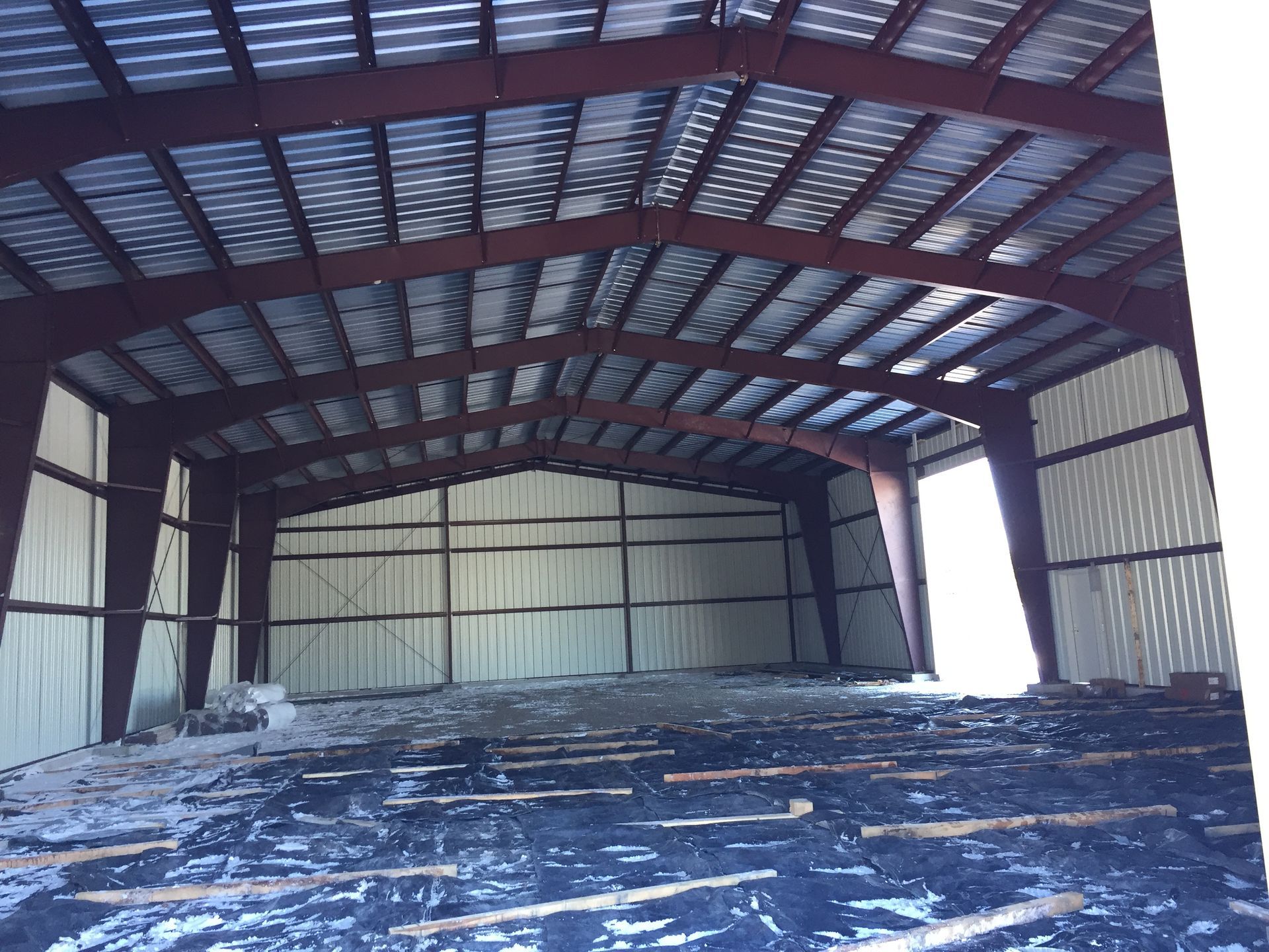 Vue intérieure d'un bâtiment à ossature métallique avec poutres rouges, toit en métal et isolation en mousse de polyuréthane projetée blanche.