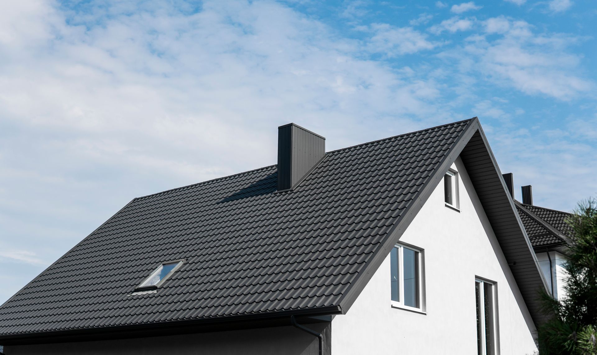 White house with dark gray tiled roof, chimney, and blue sky.