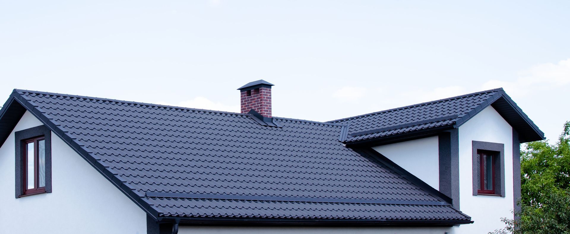 White house with a dark gray roof, two windows, and a brick chimney under a light blue sky.