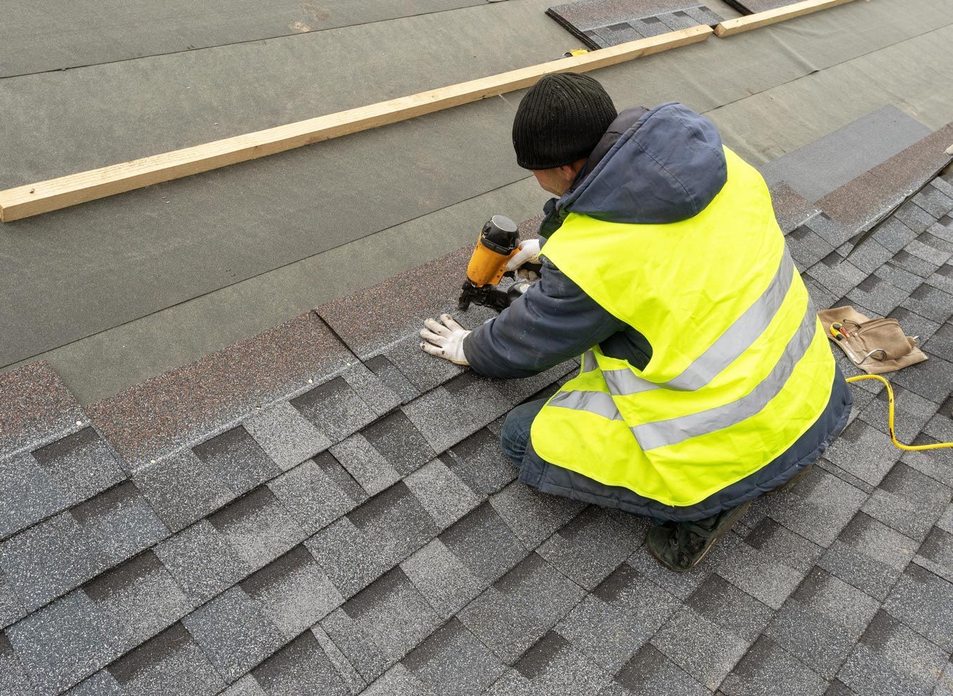 A man in a yellow vest is working on a roof