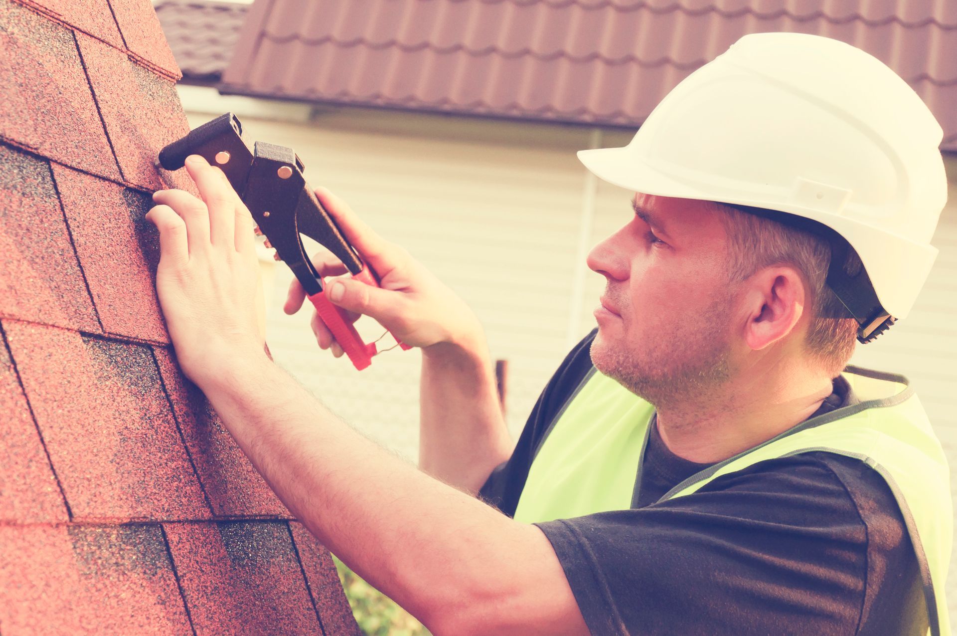 Roofing contractor installing asphalt shingles with nail gun for residential roof repair.