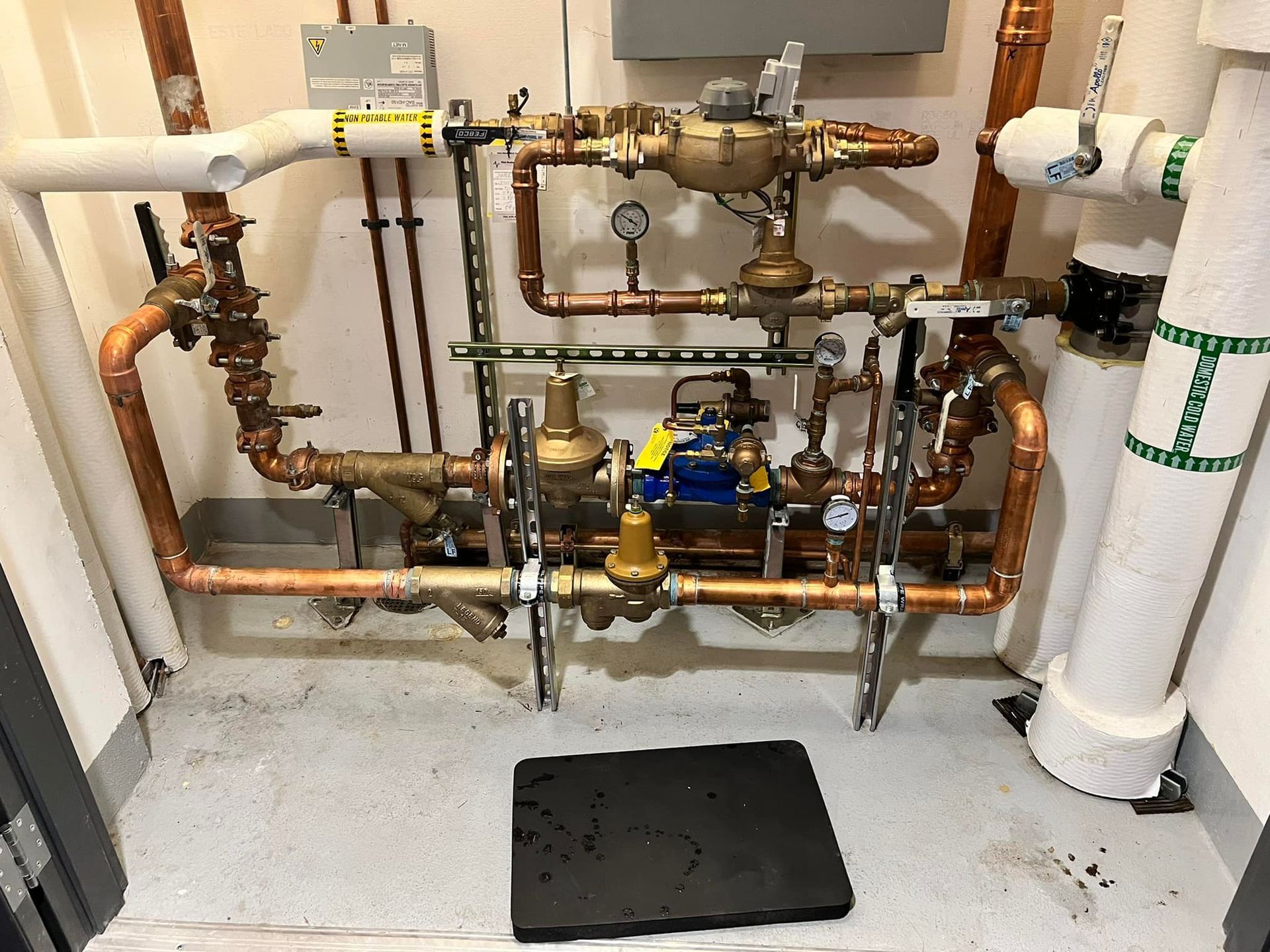 Man in blue overalls operating machinery, wearing black gloves. Inside a workshop.