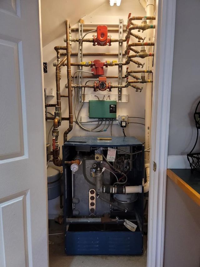 Water heaters and pipes mounted on a wall. A white tank is next to grey cylindrical tanks.
