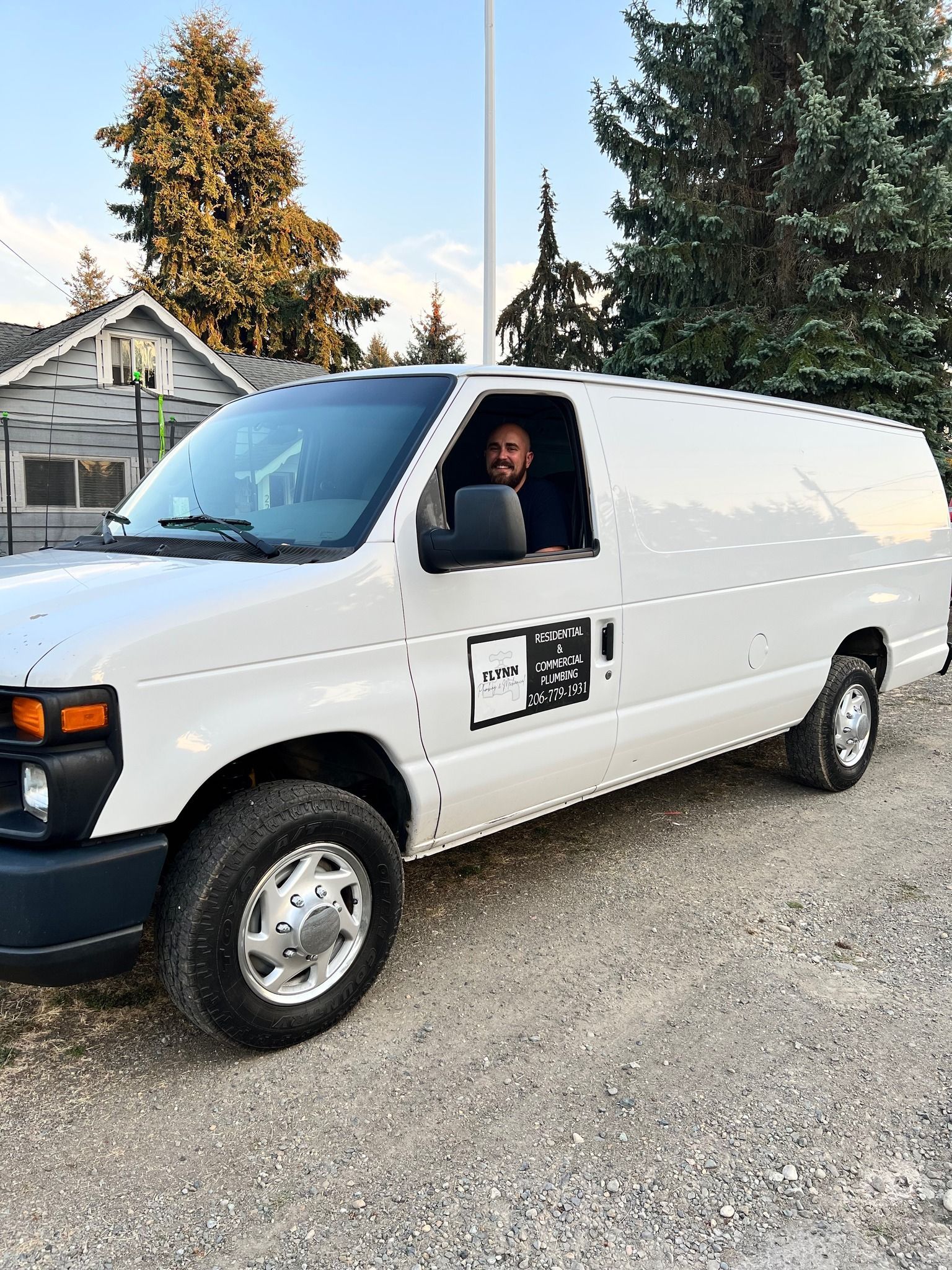 Electrician in hard hat and safety vest inspecting electrical panel, using pen, and wearing a face mask.